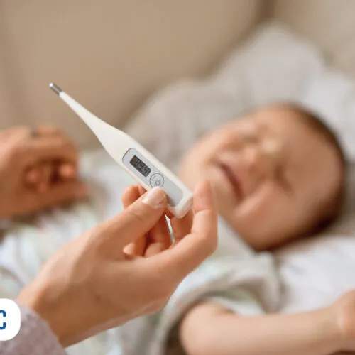 Mão segurando termômetro perto de bebê feliz.