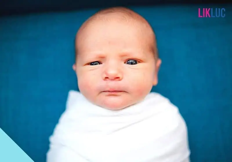 Bebe deitado e enrolado em manta, com cara de confuso