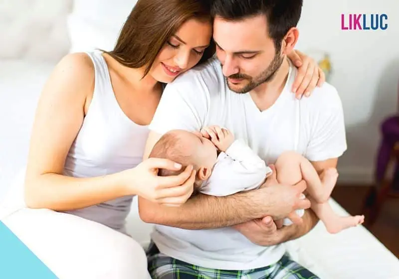 Pais segurando neném no colo, com mão na cabeça moleira do recém-nascido