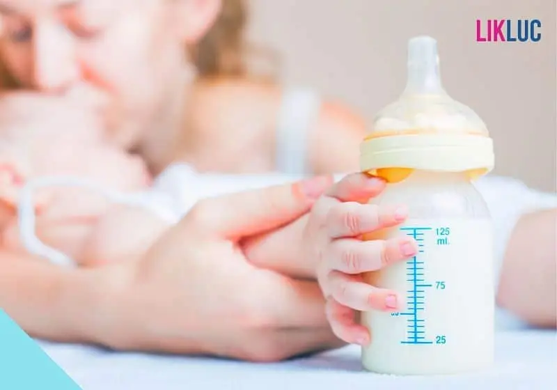 mamãe beijando a testa do bebê que esta dormindo segurando sua mamadeira