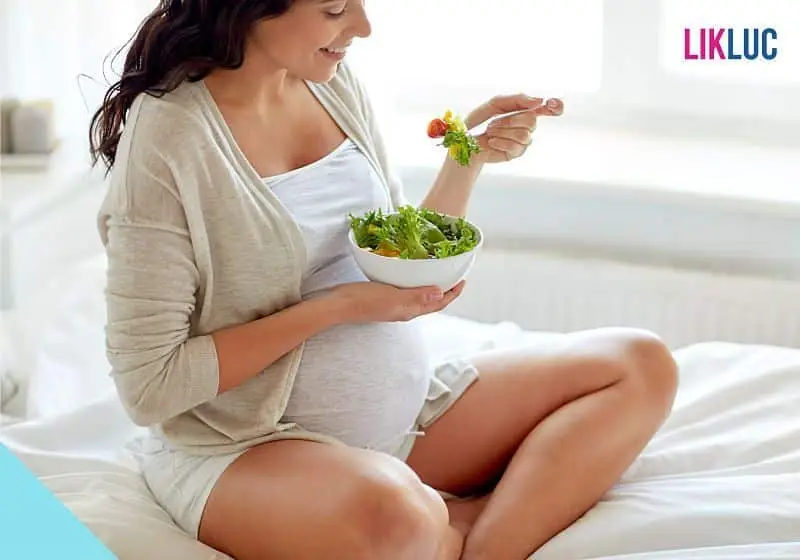 gestante sentada na cama comendo um bowl com legumes e verduras