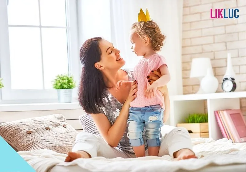 mae segurando filha enquanto sorri mae sentada na cama segurando filha enquanto sorri