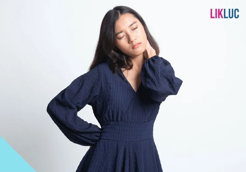 Mulher com um vestido azul marinho, com seu braço esquerdo no pescoço e com expressão de dor de pescoço