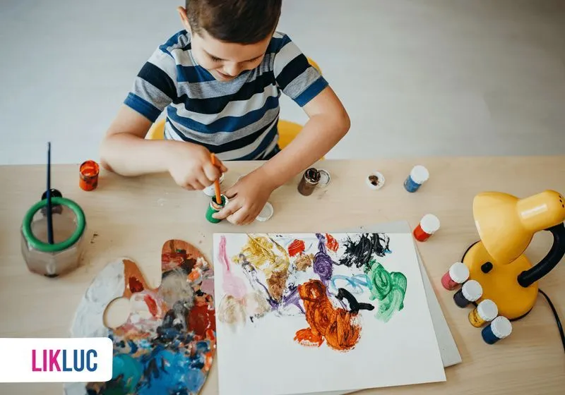 Brincadeiras para fazer junto a crianca menino brincando de pintura em papel com varias tintas a mesa