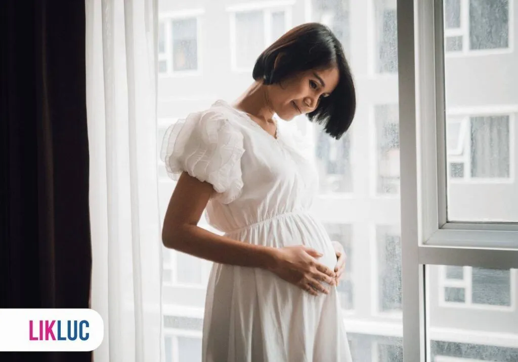 Gestante vestindo um vestido branco e com as mãos sobre a barriga