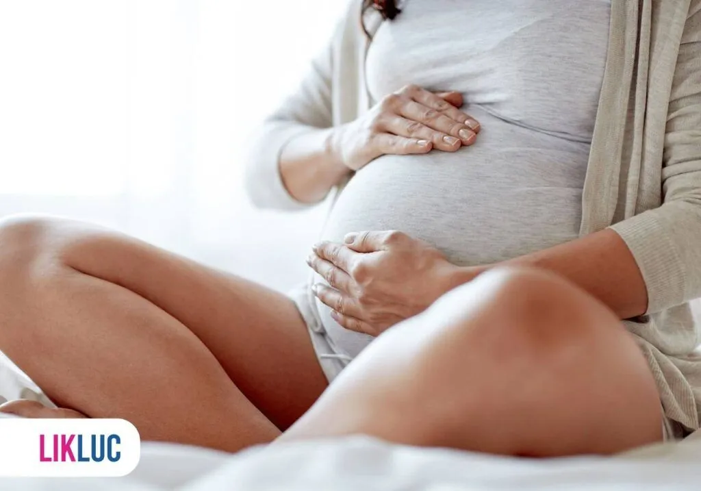 Gestante sentada segurando a sua barriga com as duas mãos