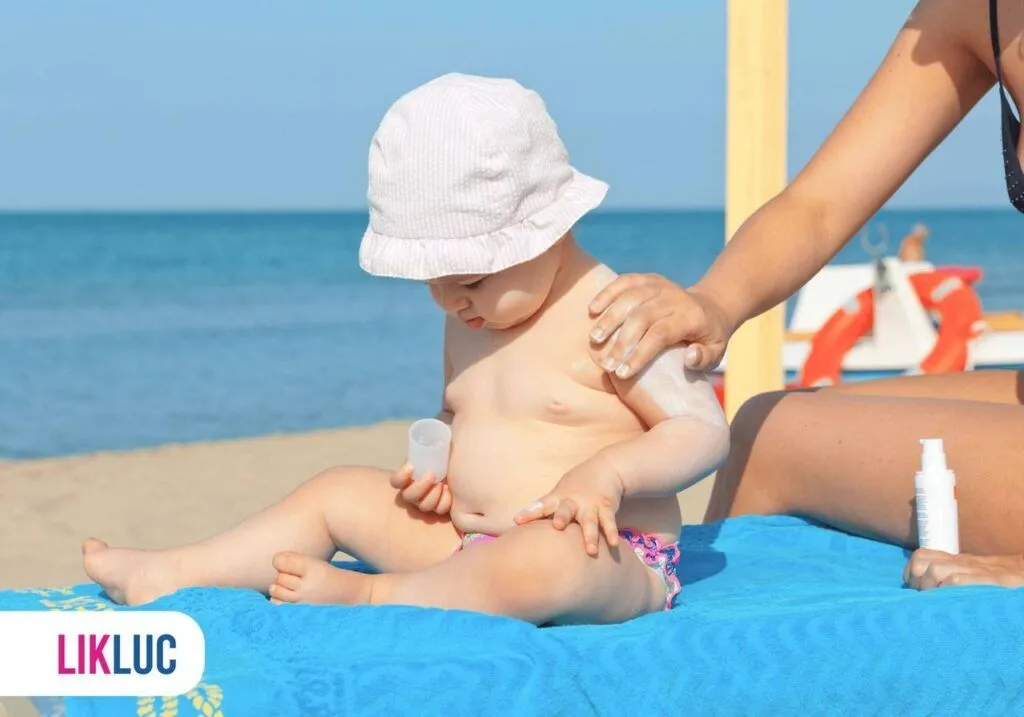 mamãe passando protetor solar em um bebe sentado na areia da praia
