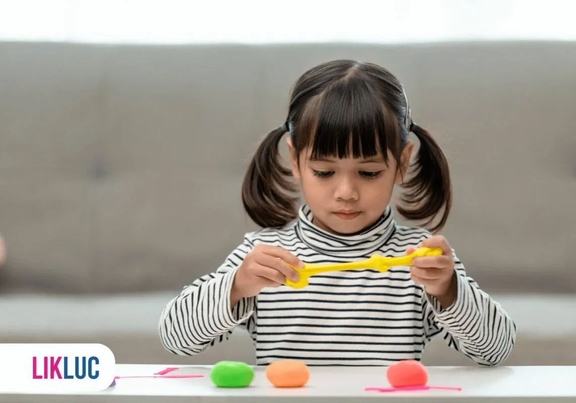 Vista de frente de uma criança fazendo formas com massinha de modelar colorida em cima da mesa