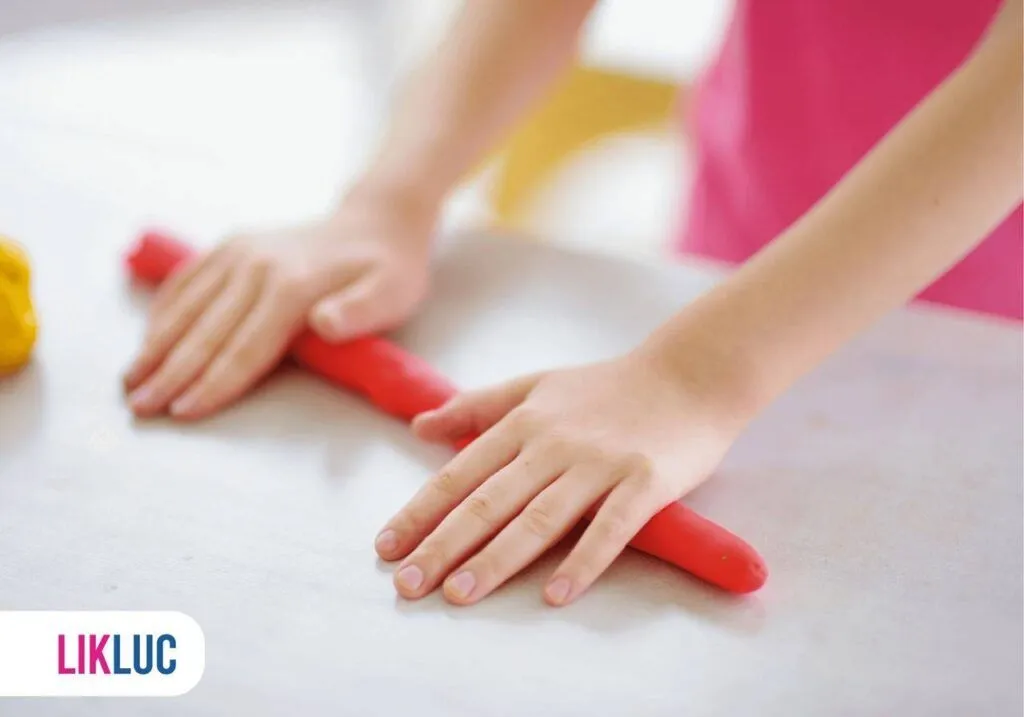 vista lateral das mãos de uma criança fazendo um roinho de massinha de modelar em cima da mesa