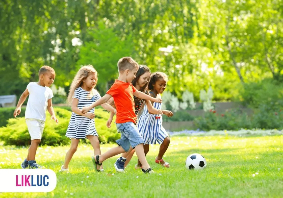 Cinco crianças brincando de jogar futebol, correndo sobre a grama