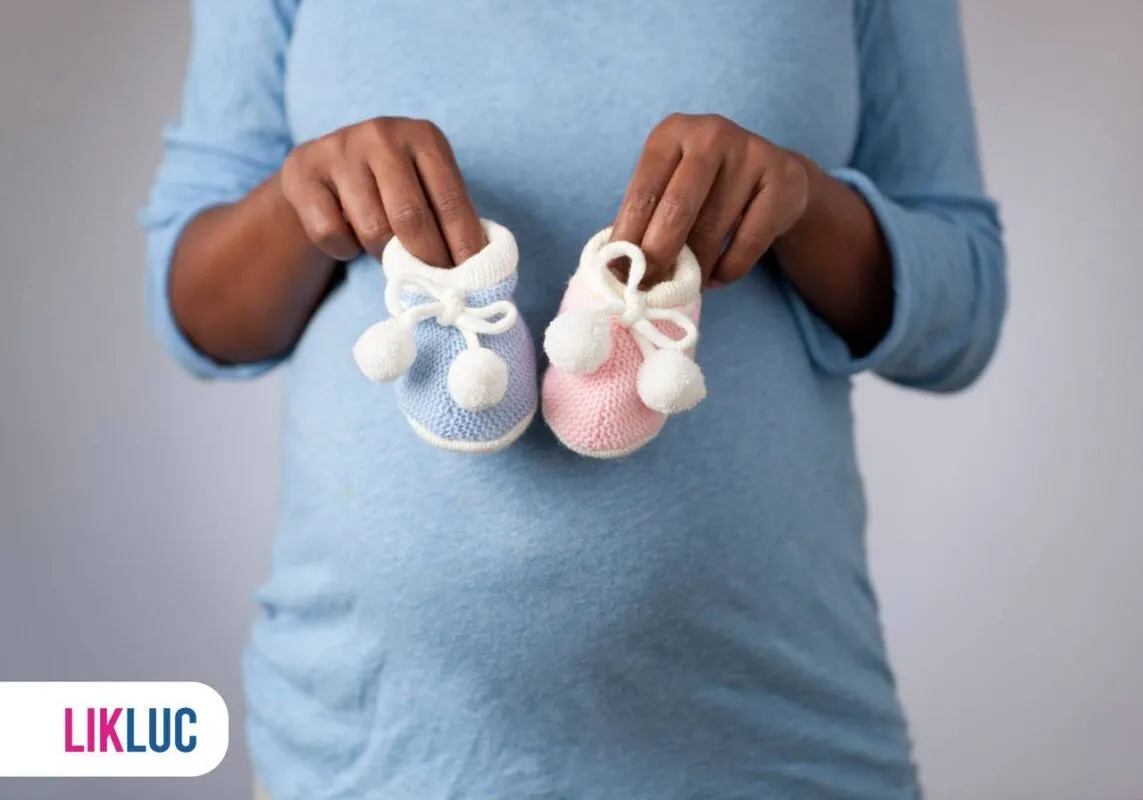 Grávida segurando sapatinhos de bebê, um rosa e um azul