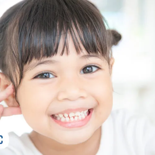 Criança sorridente com cabelos presos e dedos na bochecha