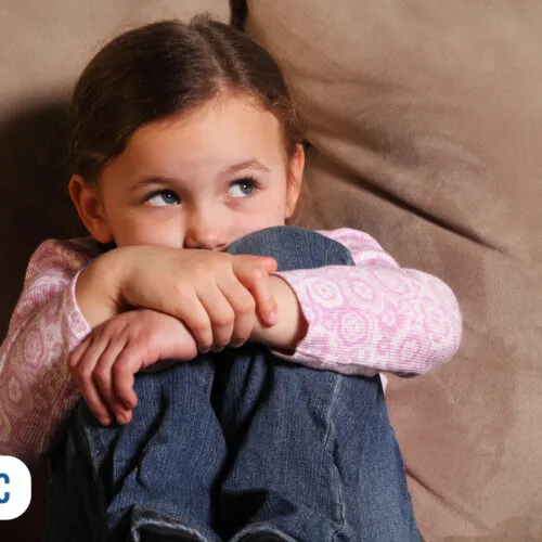 Criança encolhida em sofá, olhando para o lado.