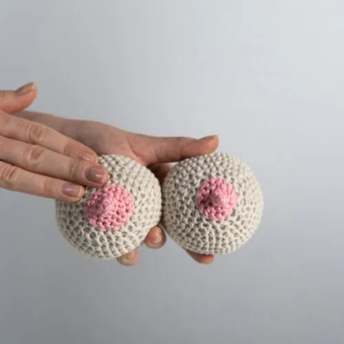 Mãos segurando peças de crochê em formato de seios.