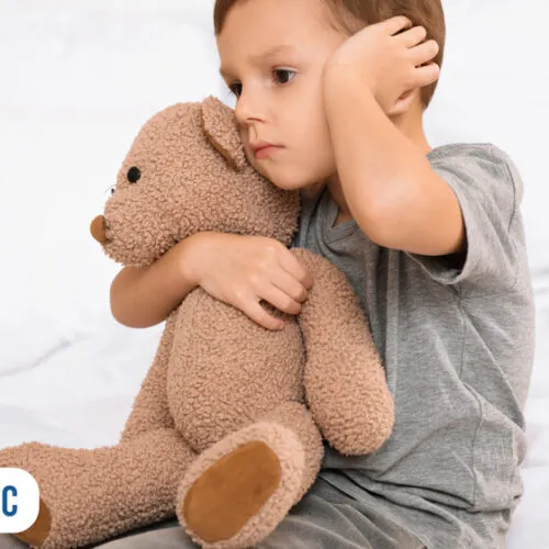 Criança abraçando urso de pelúcia e parecendo triste.